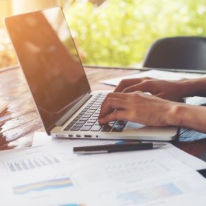 Business woman hand typing on laptop keyboard with Financial charts on the table. Working at her home.